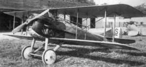 Photo of a single-engine bi-wing aircraft with an open cockpit. It is parked on grass.